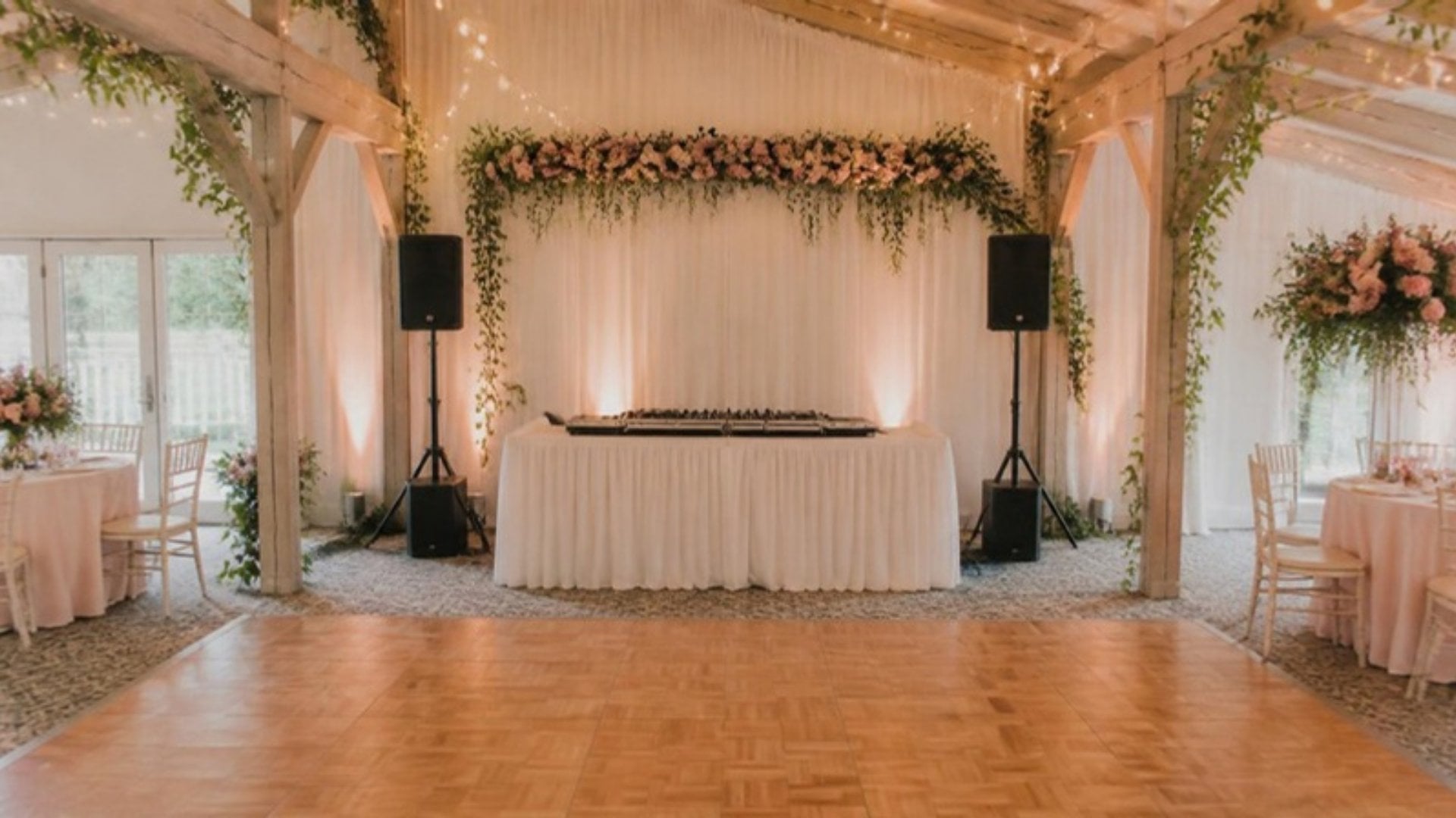Platine DJ et enceintes installées devant une piste de danse de mariage décorée de fleurs et de guirlandes lumineuses